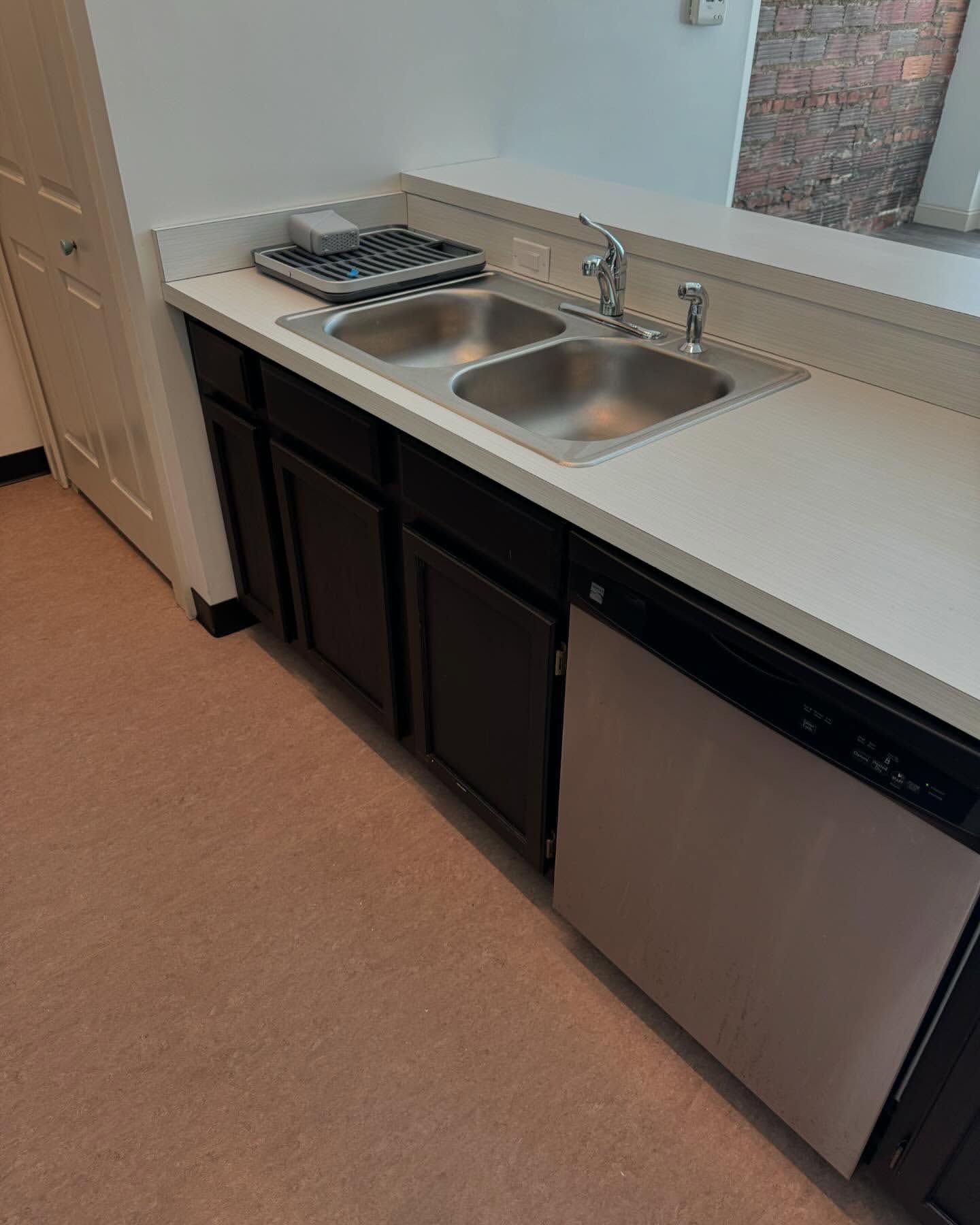 Kitchen with double sink, black cabinets, and white countertop. Dishwasher is visible. Beige carpet.