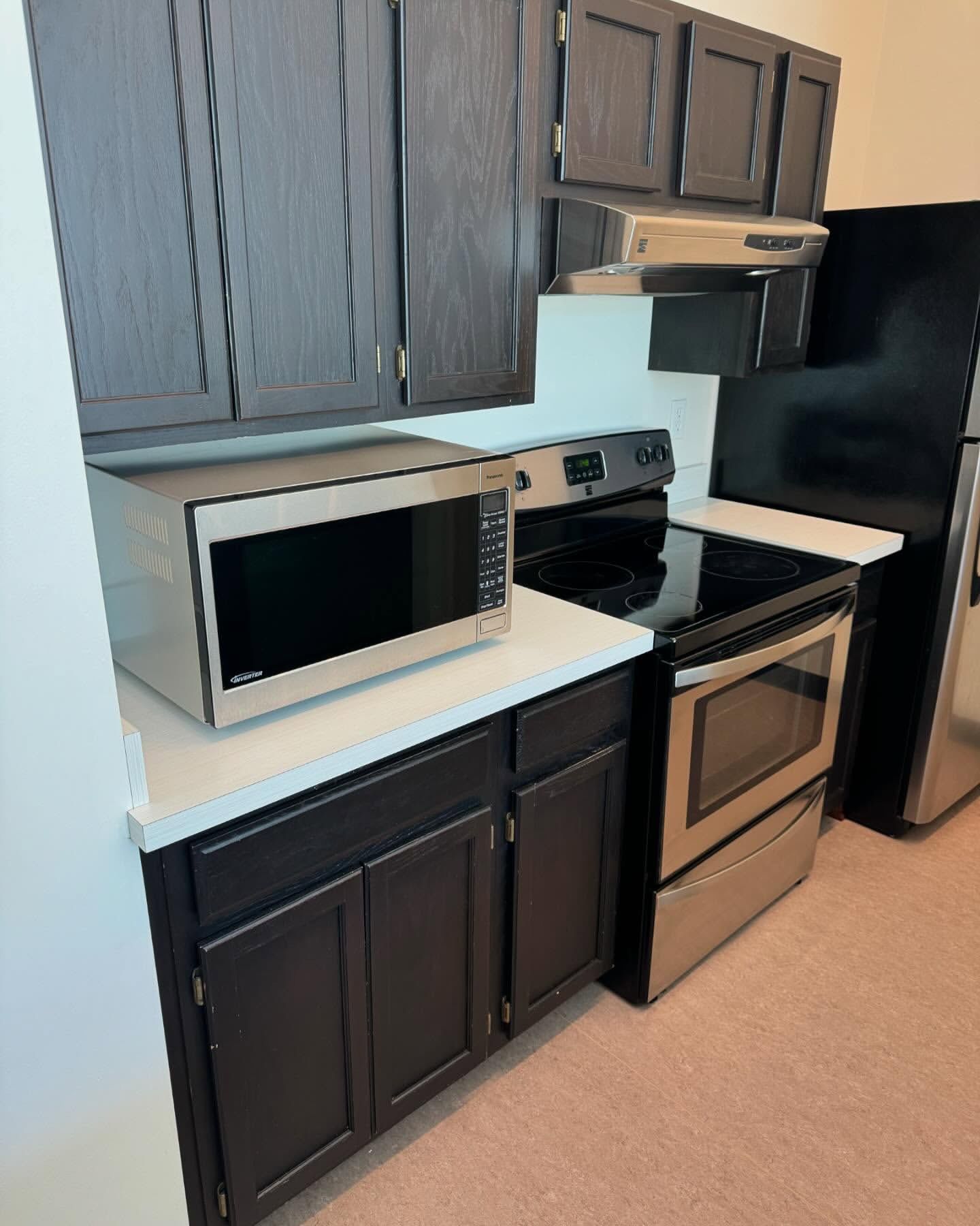 Kitchen with dark cabinets, stainless steel appliances, including a microwave and oven.