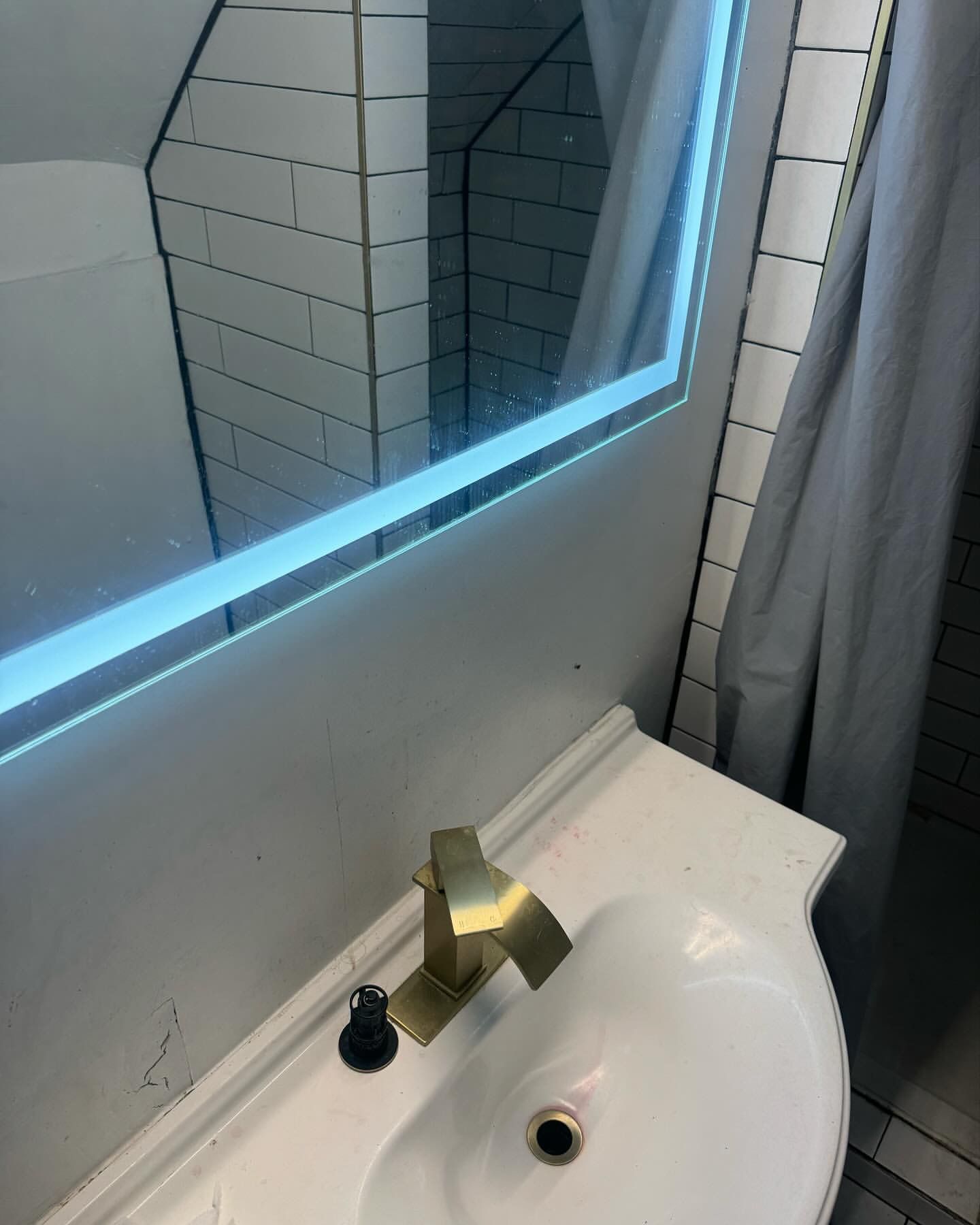 Bathroom sink with a gold faucet, lit mirror, and white tiles.