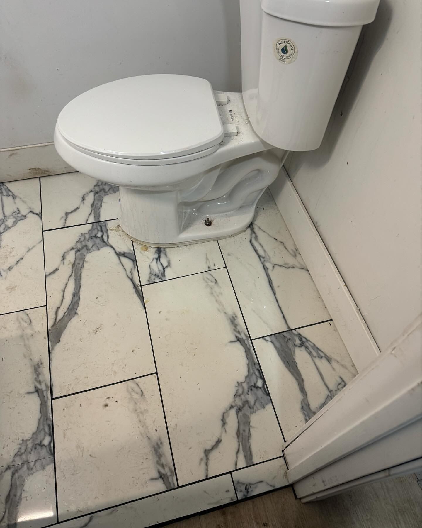 Toilet on marble-look tile floor in a bathroom corner. White toilet and seat, gray veins in the tile.