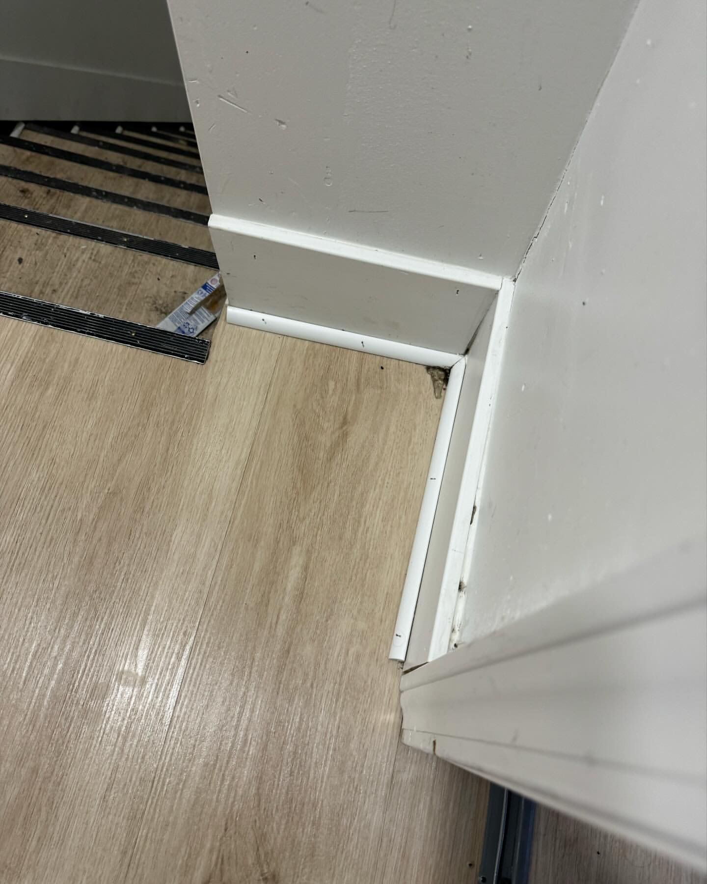 White baseboards meet at a corner on a light wood-grain floor, a white wall is to the right.