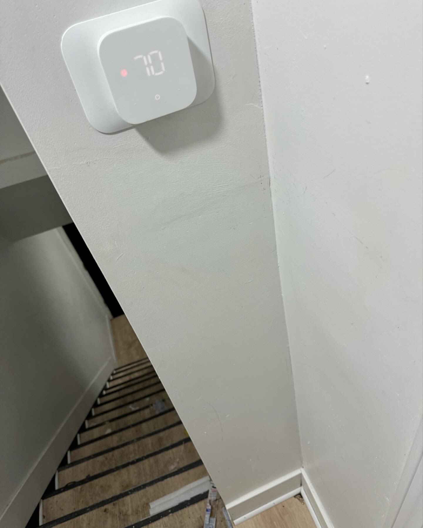 A Nest thermostat displaying 70 degrees on a white wall next to a staircase.
