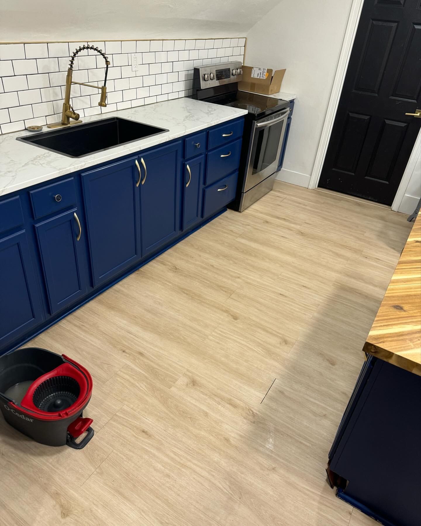 A small kitchen with blue cabinets, a black sink, and light wood-look flooring.
