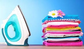 Iron next to a colorful stack of folded laundry, topped with flowers, on a blue background.