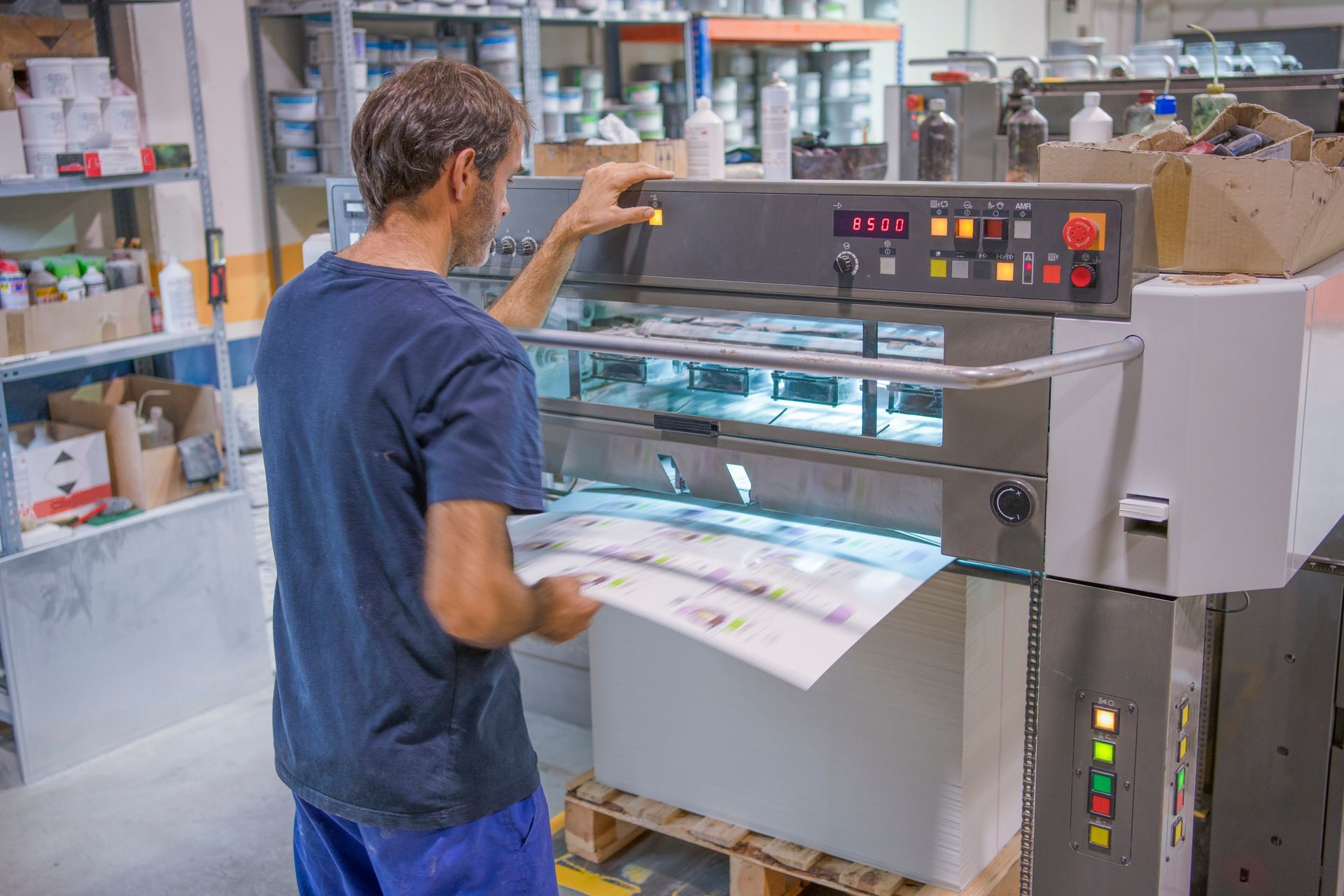 A man, handling a huge offset printer, checks the results of the printing and cutting quality. A man, handling a huge offset printer, checks the results of the printing and cutting quality.