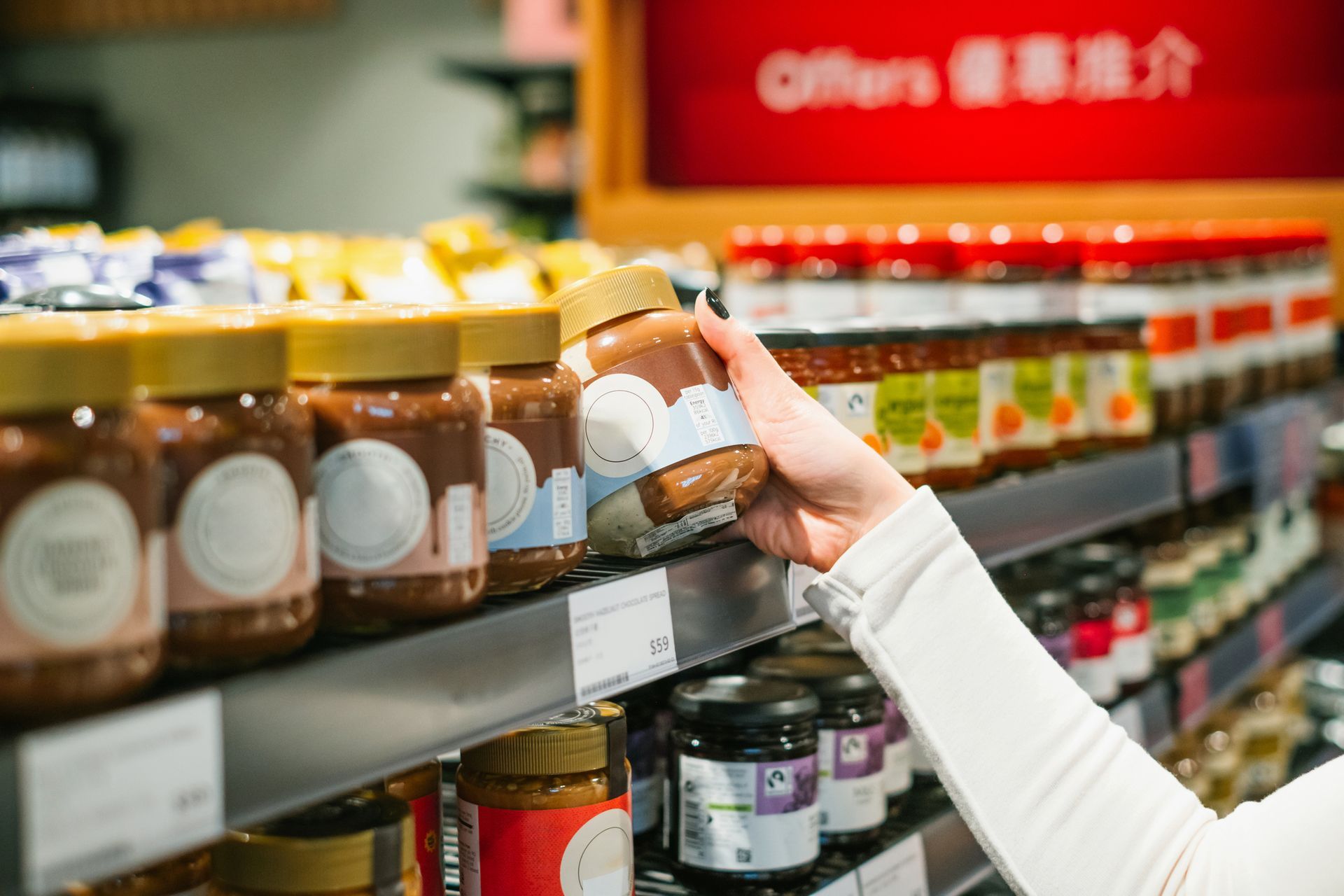 A person is holding a jar of peanut butter in a grocery store.