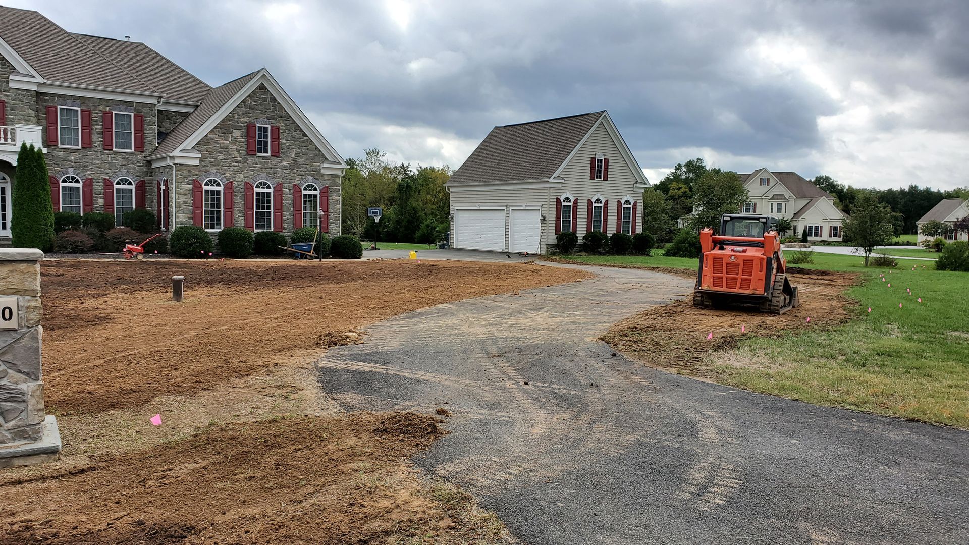 A tractor is driving down a dirt road in front of a house.
