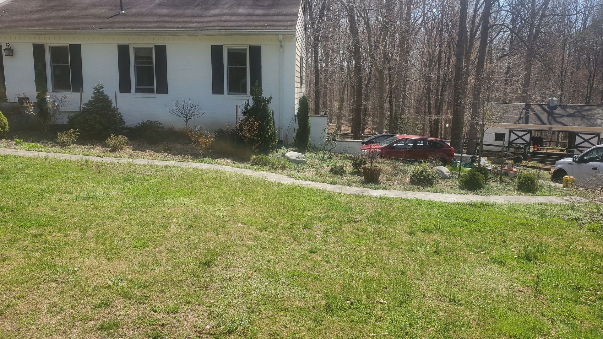 A white house with black shutters is surrounded by trees and grass