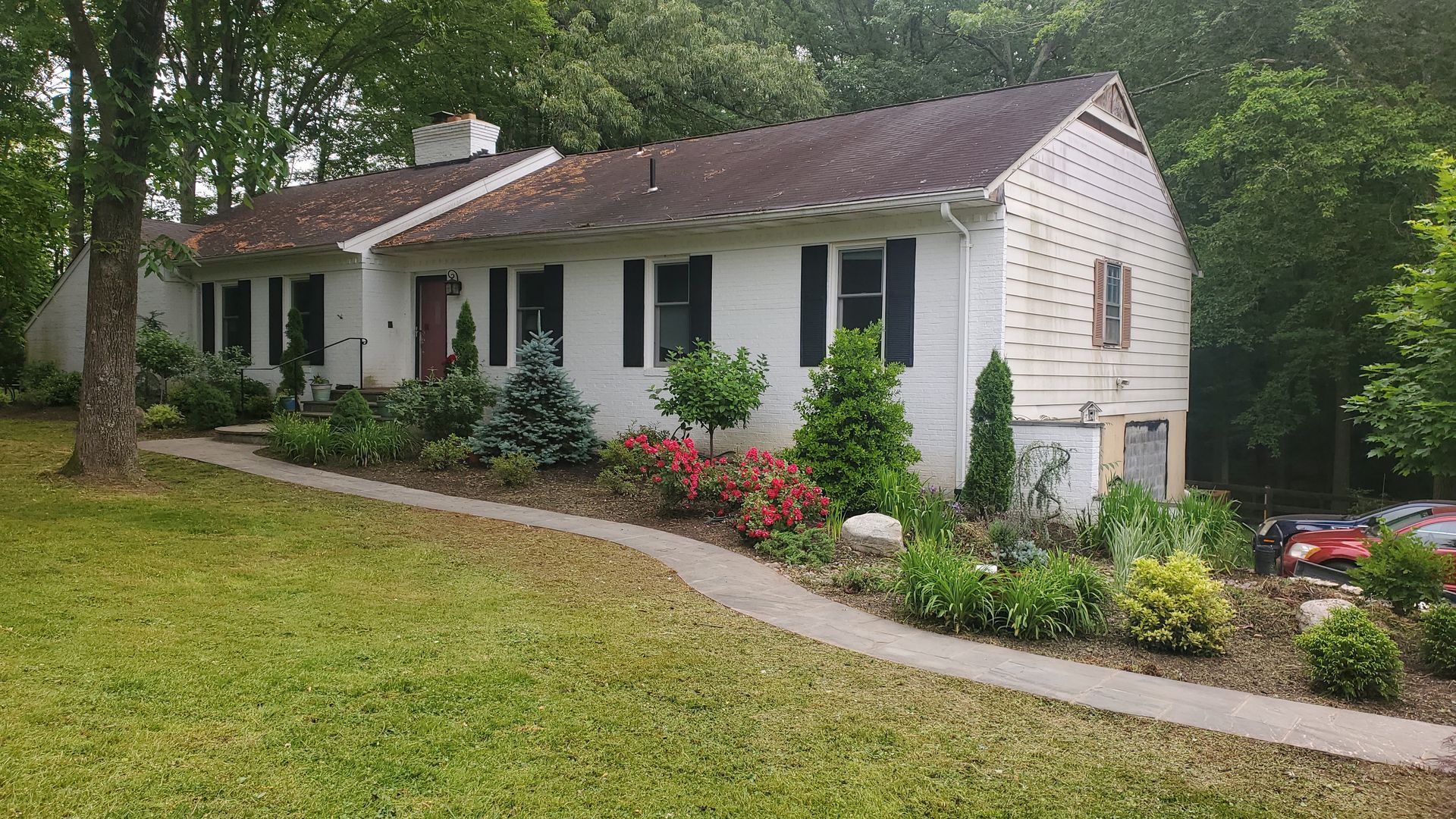 A white house with a brown roof is surrounded by trees and bushes