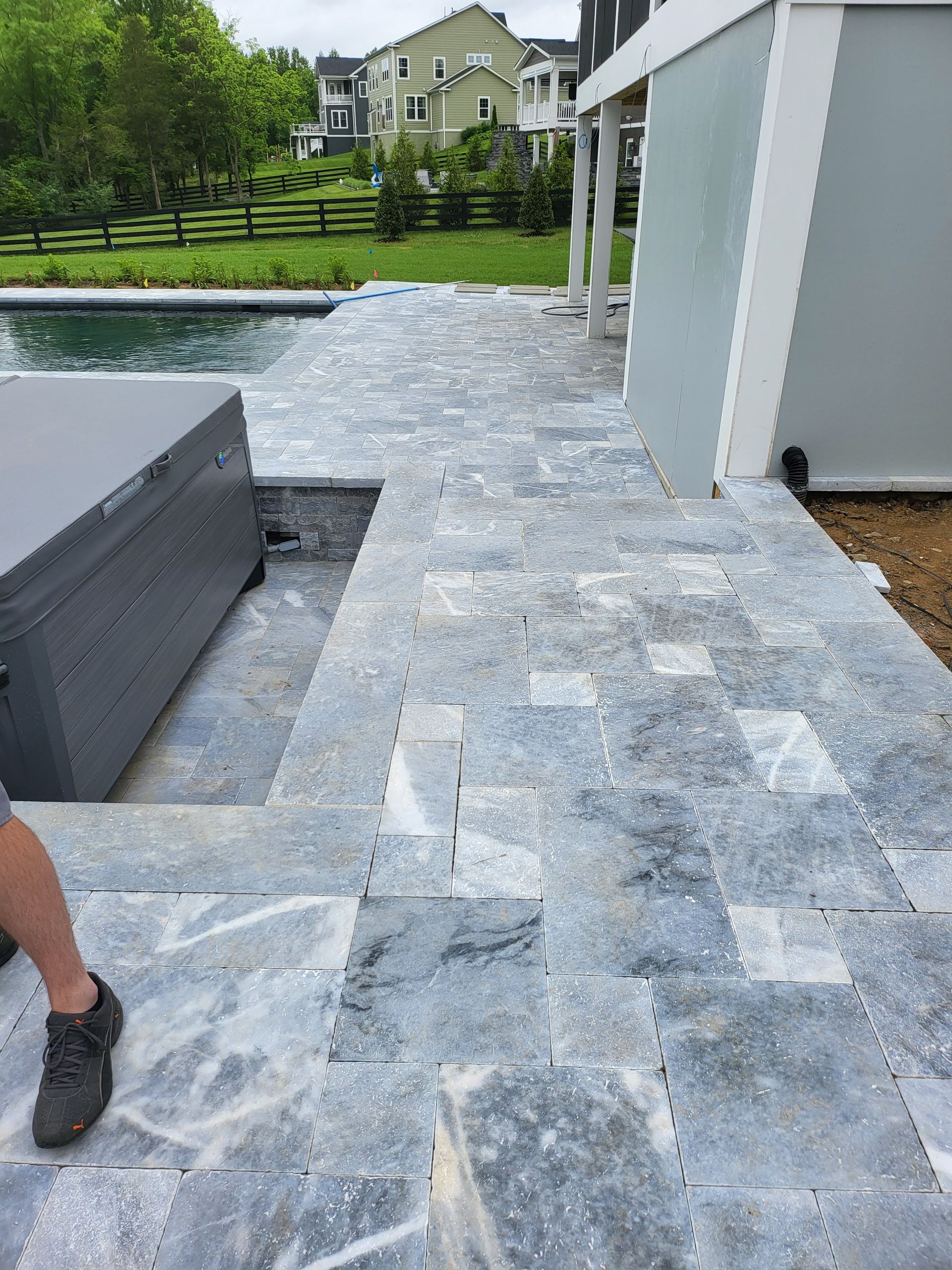 A person is standing on a patio next to a pool.