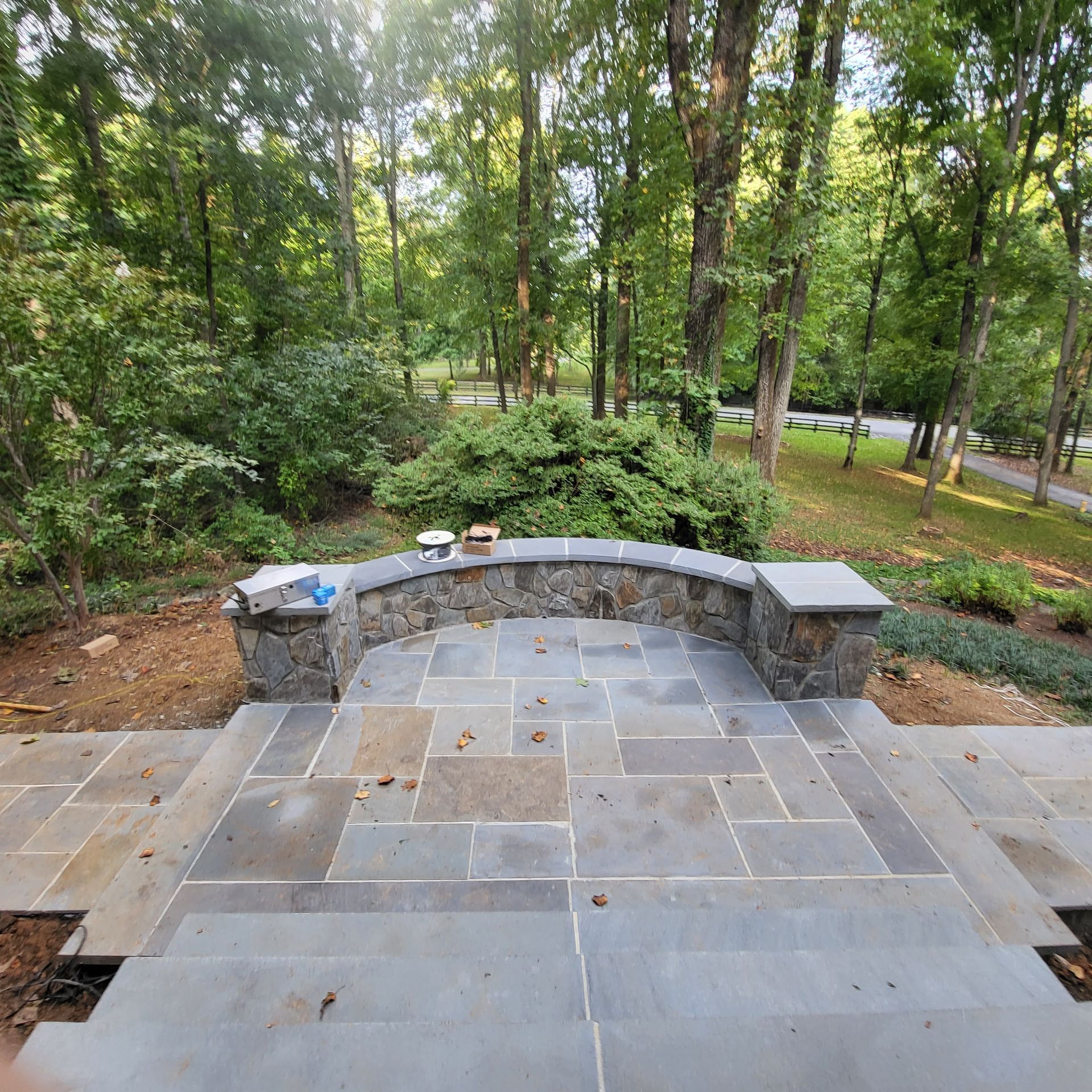 A patio with a stone wall and steps leading to a forest
