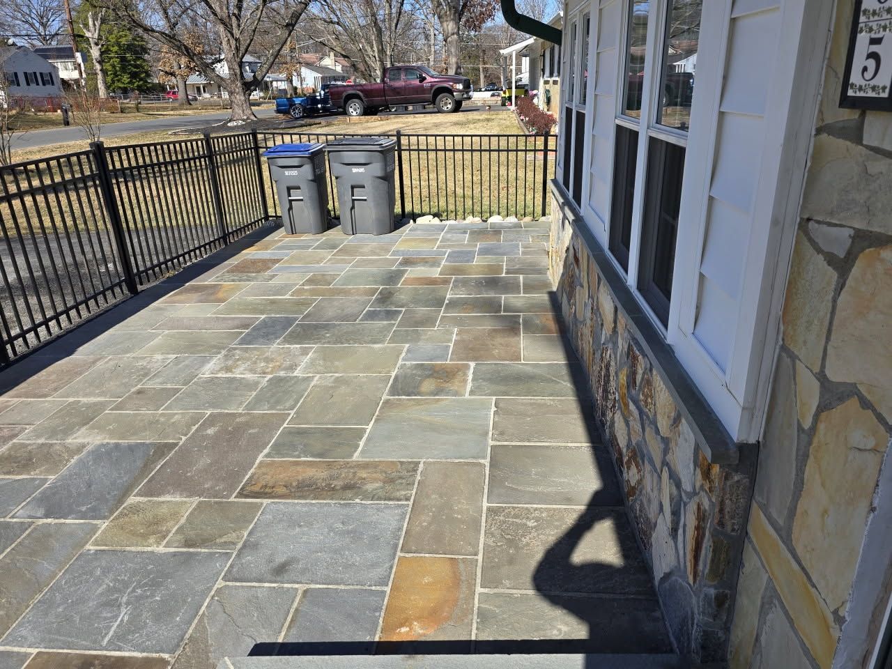 A stone patio with a fence and trash cans in front of a house
