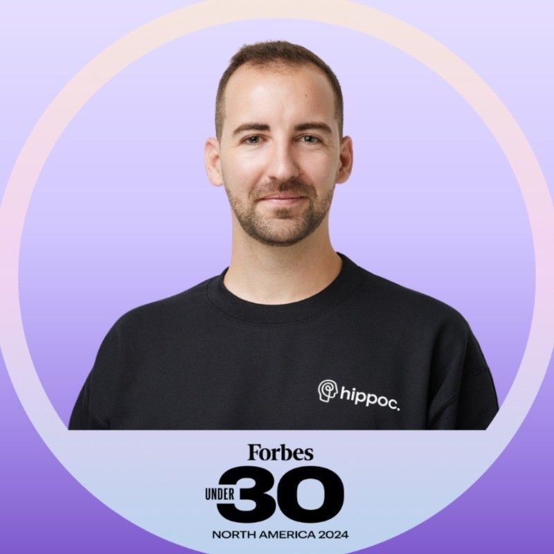 A man wearing glasses and a blue suit is standing in front of a white background.