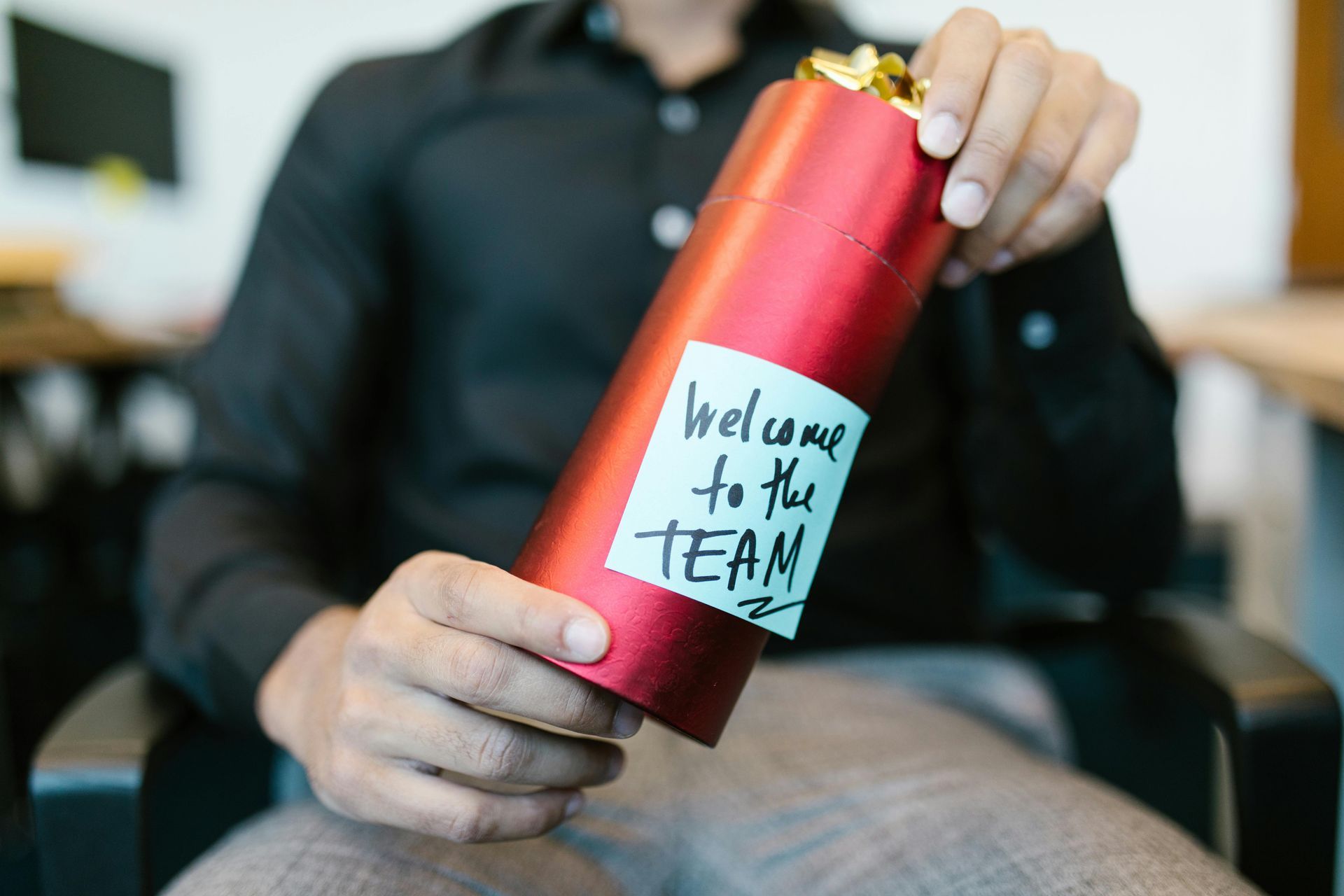 A man is holding a red gift box with a welcome to the team sticker on it.