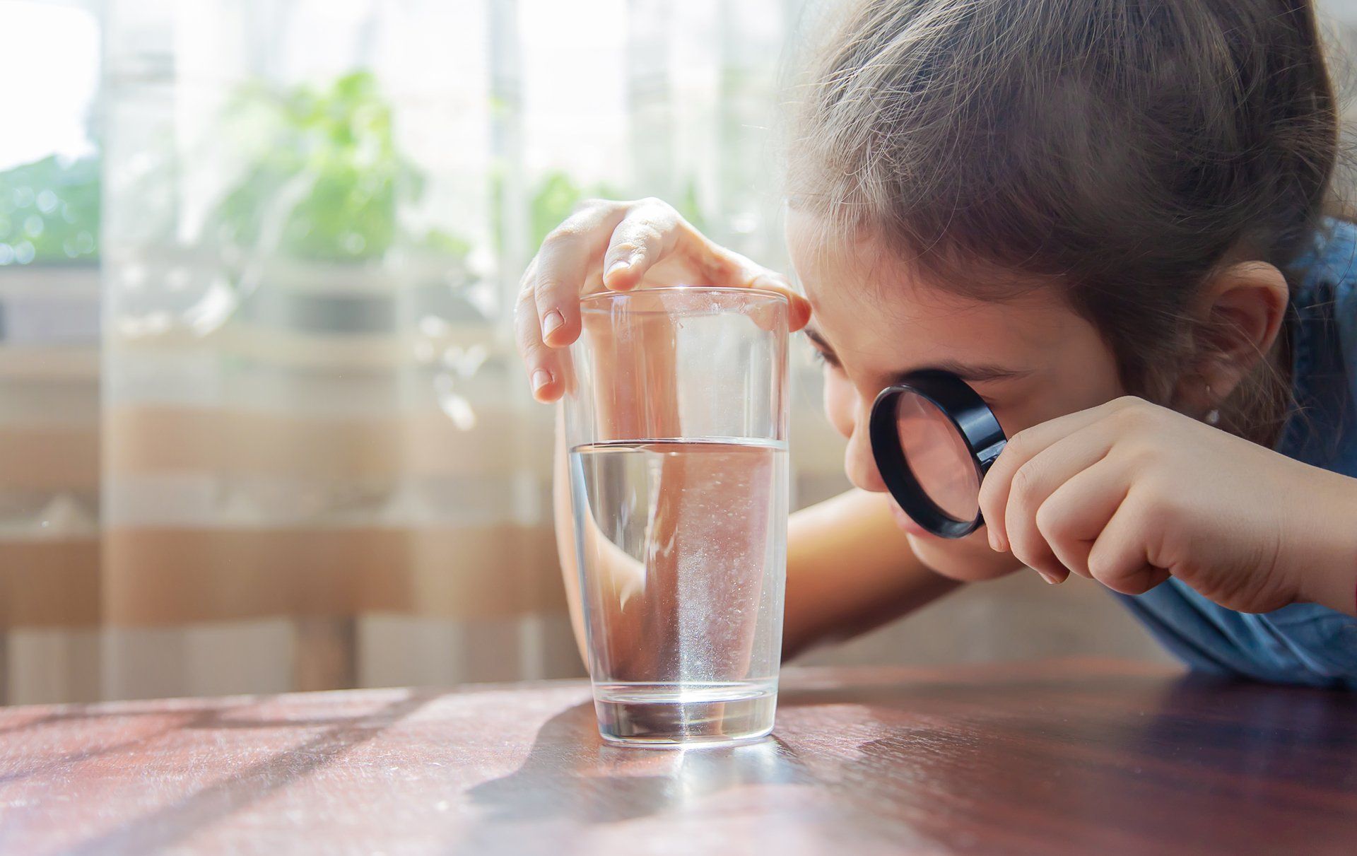 The child examines the water with a magnifying glass in a glass.