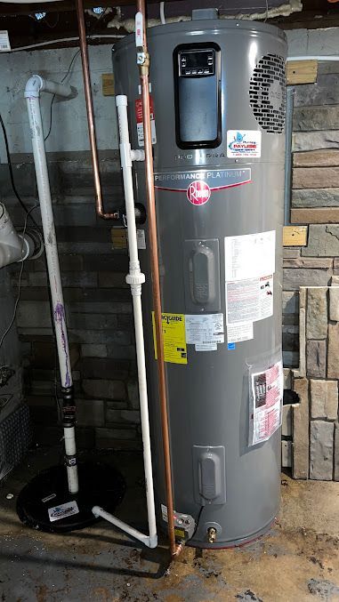 A gray water heater is sitting in a basement next to a brick wall.