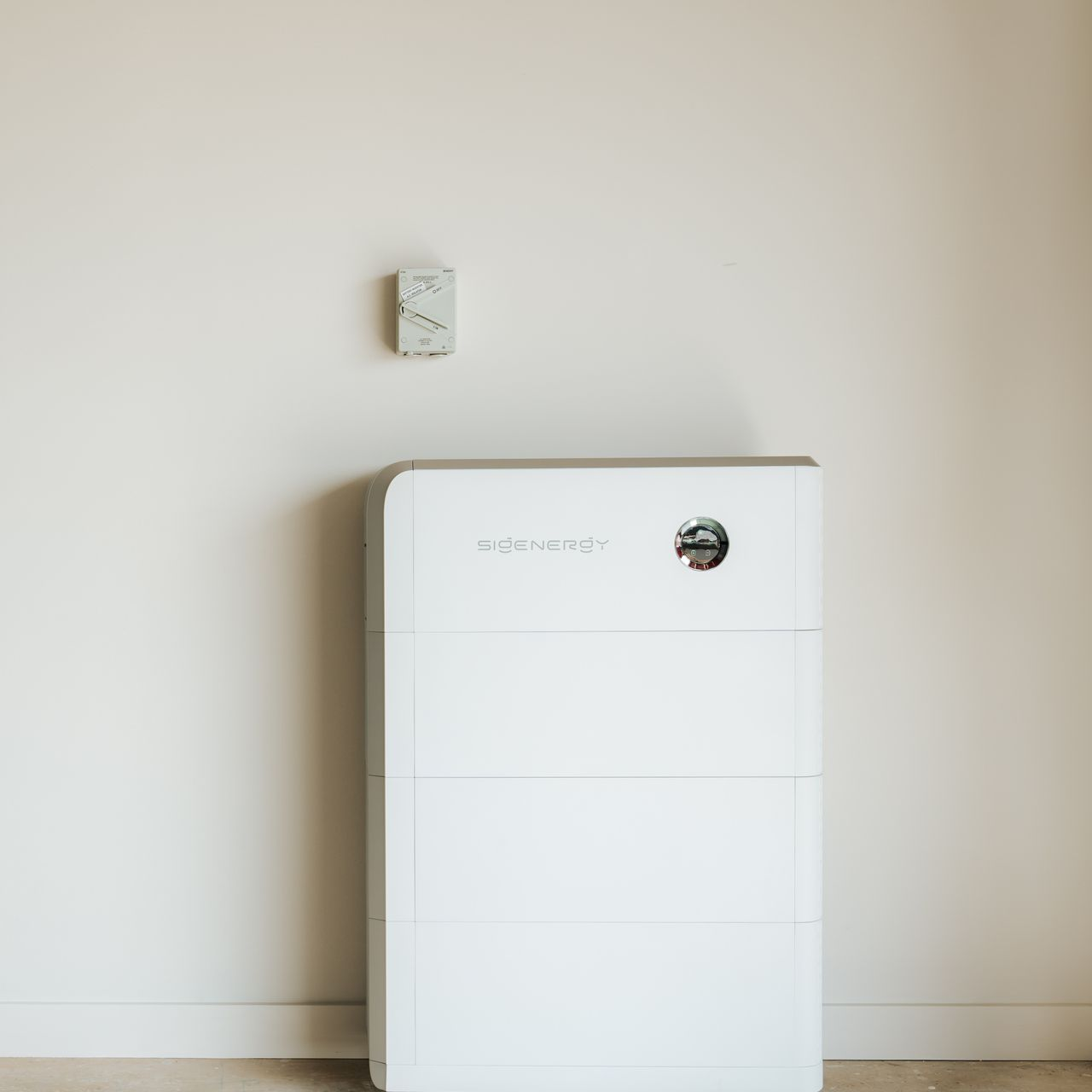 White home energy storage system and wall-mounted control panel against a plain wall.