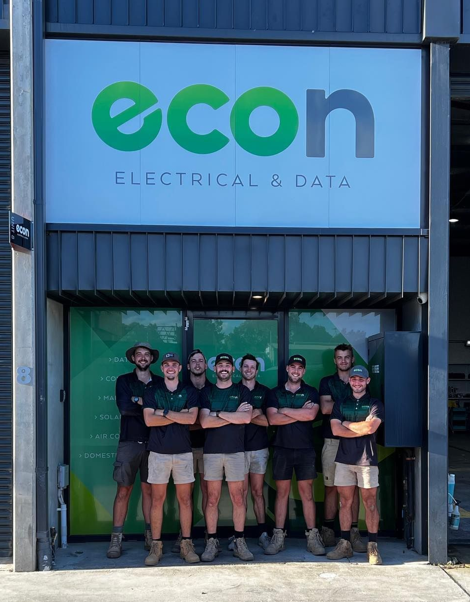 Econ Energy team posing in front of a store logo named Econ Electrical & Data