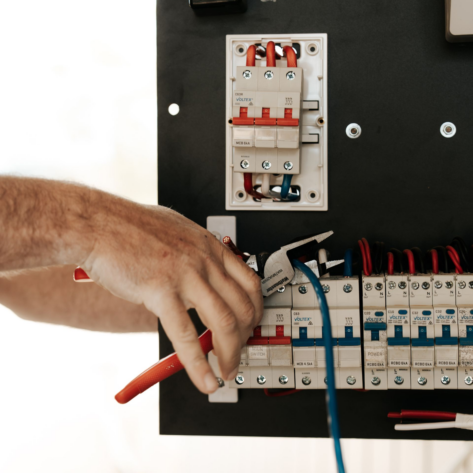 Electrician using pliers on wires in a circuit breaker panel.