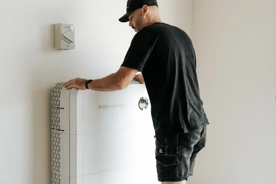 Man installing a white rectangular object on a white wall; other items visible.