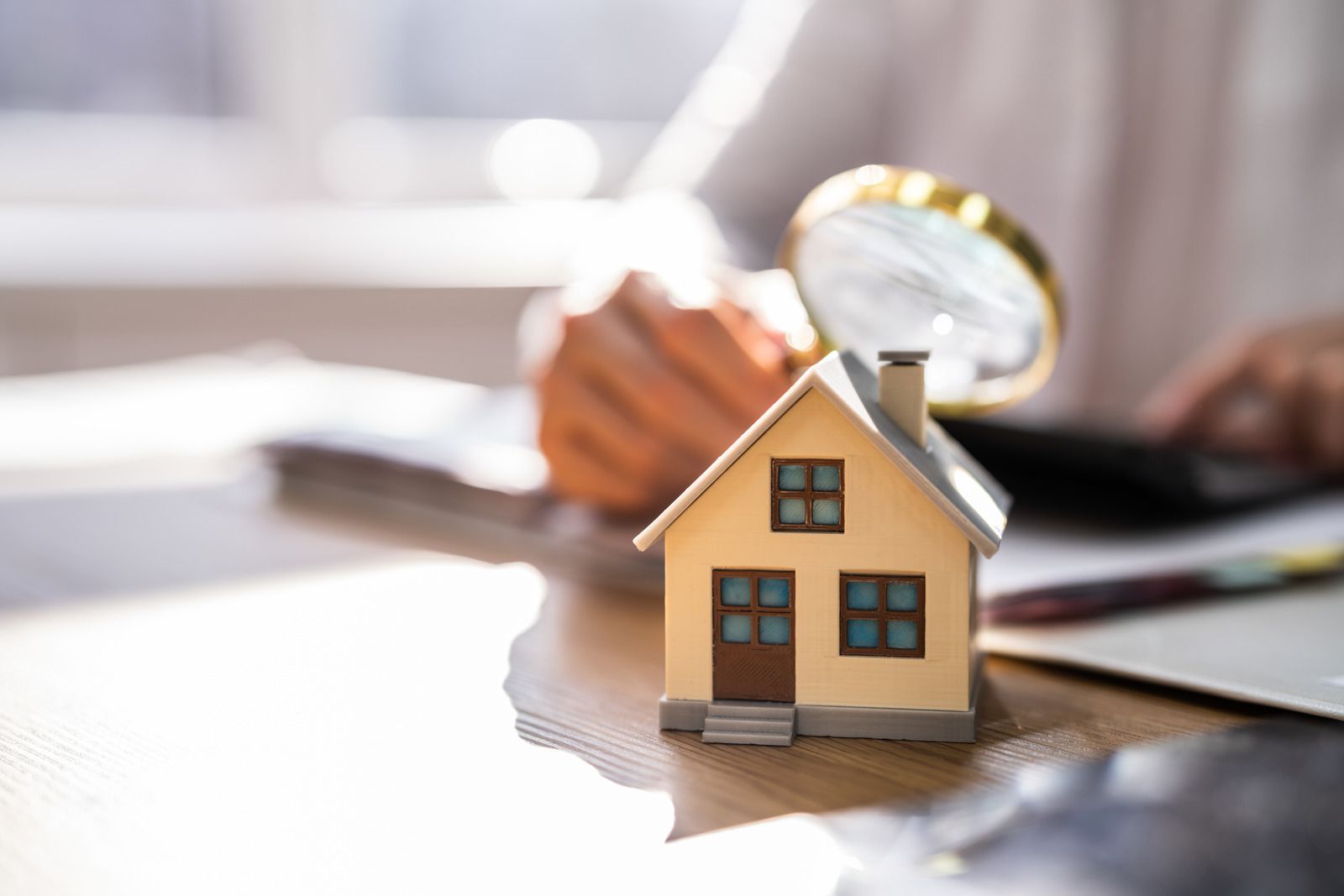 A person is holding a magnifying glass over a model house on a table.
