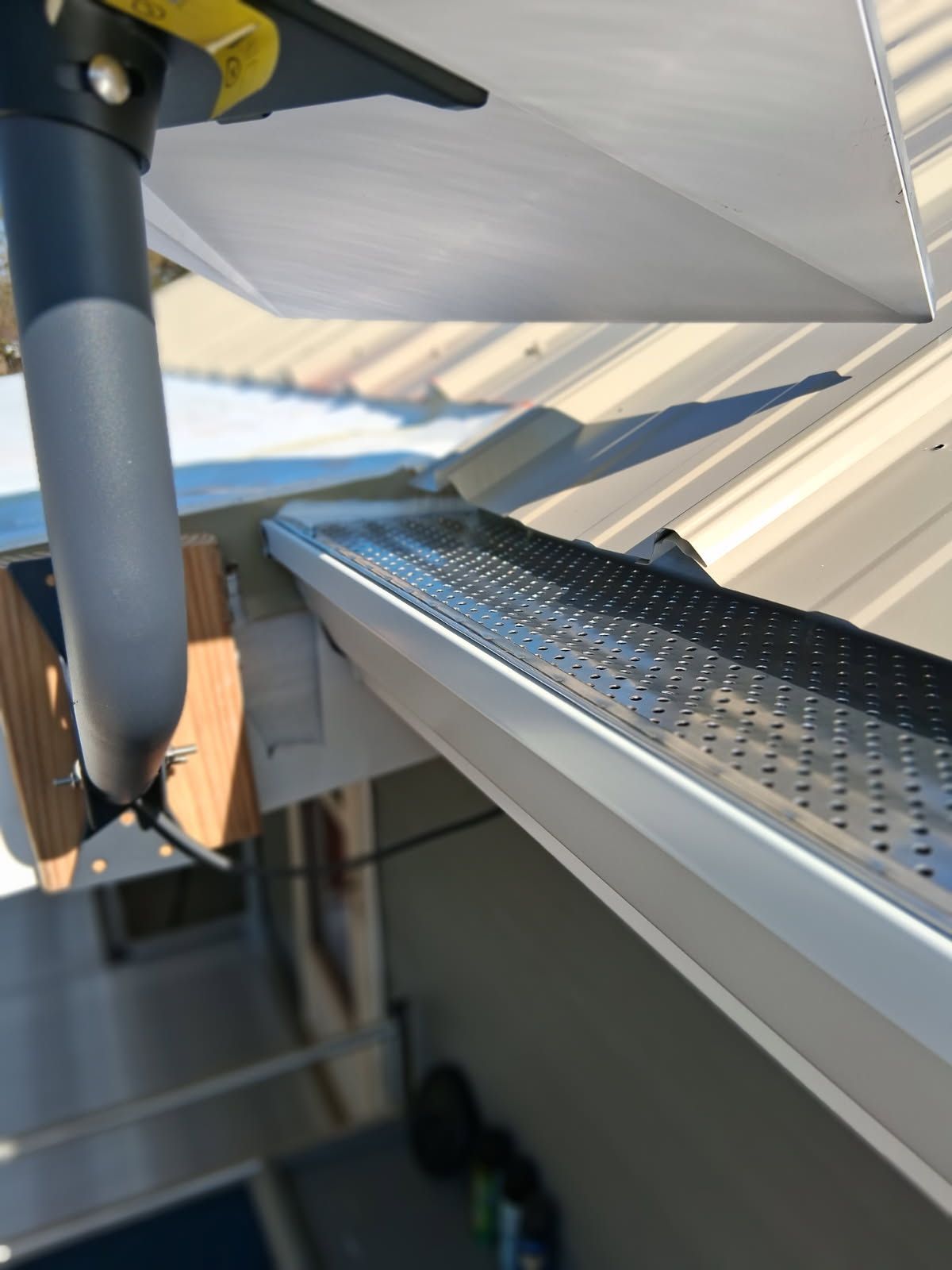 Gutter with metal mesh, downspout, and metal roof.
