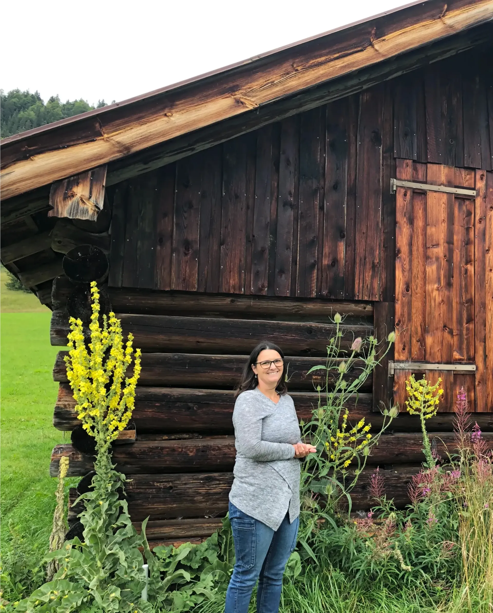Eine Frau steht vor einer Blockhütte auf einem Feld.