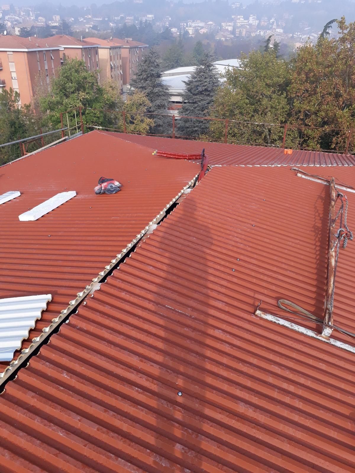 Tetto in lamiera ondulata rossa in fase di ristrutturazione, sulla cui superficie si proietta la lunga ombra di una persona.
