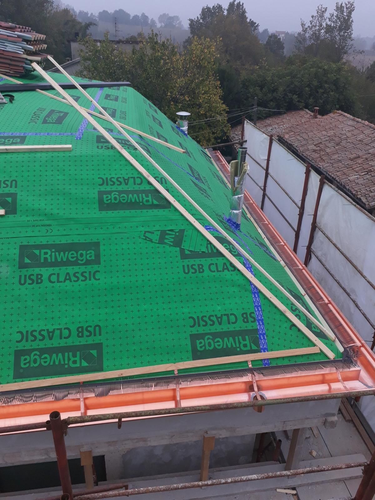 Un tetto in costruzione ricoperto con sottostrato Riwega USB Classic di colore verde, con listelli di legno e grondaie già installati.