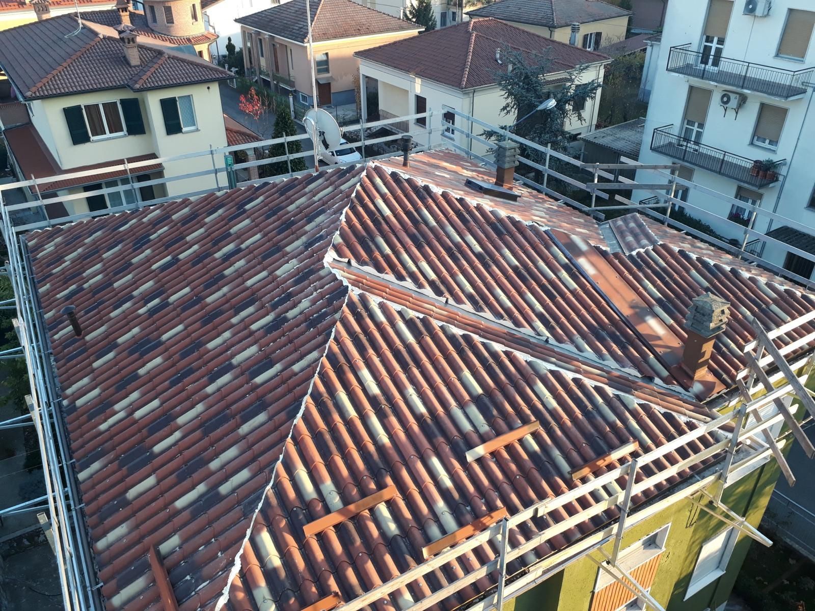 Vista dall'alto di un tetto di tegole in fase di ristrutturazione, circondato da impalcature, in un quartiere residenziale.