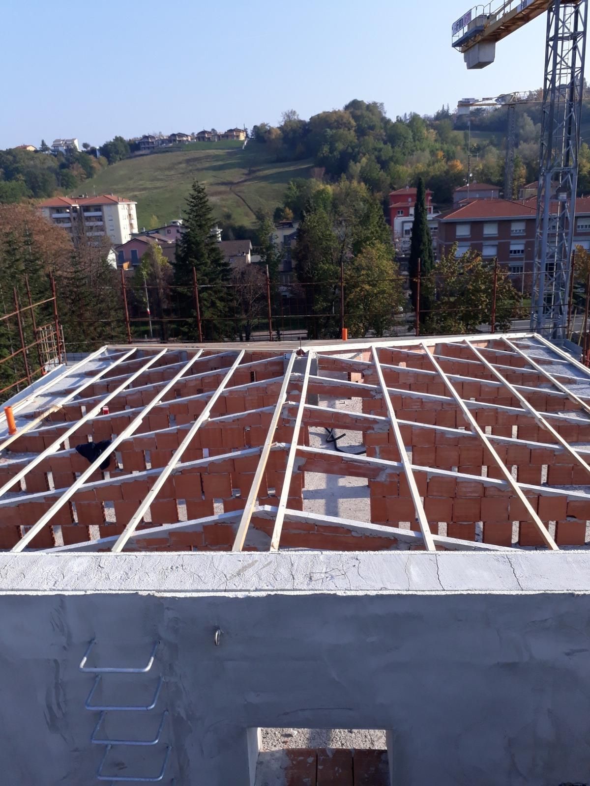 Vista di un cantiere edile che mostra la costruzione di un pavimento con una griglia di travi di legno e mattoni cavi di argilla di colore bruno-rossastro.