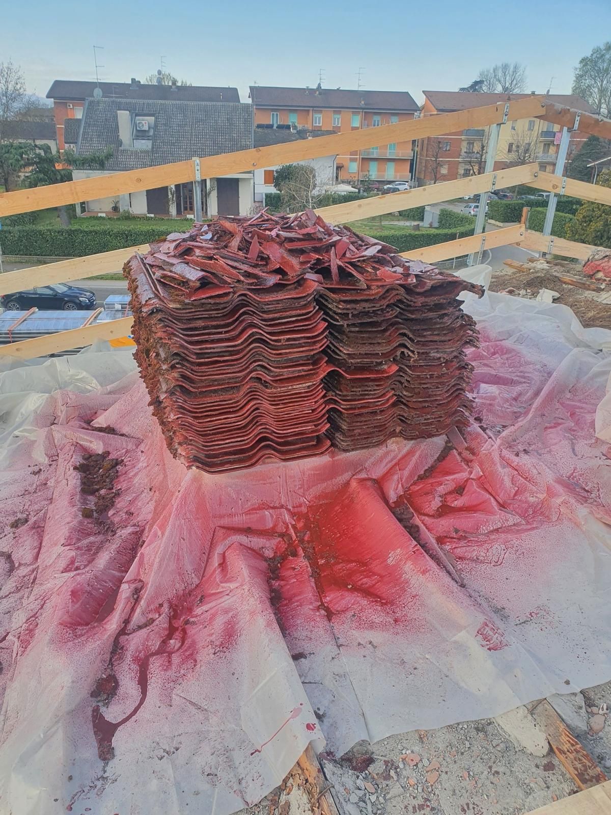 Una pila di tegole rosse è appoggiata su un telo bianco in un cantiere edile sul tetto di un'abitazione.
