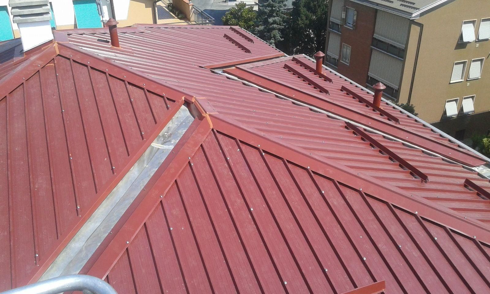 Vista dall'alto di un tetto in metallo rosso con diverse sezioni inclinate, tubi di ventilazione e paraneve.