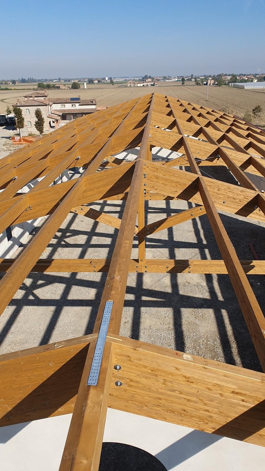 Una ripresa dall'alto che mostra la struttura di un tetto in legno in costruzione, sullo sfondo di un cielo azzurro e limpido.