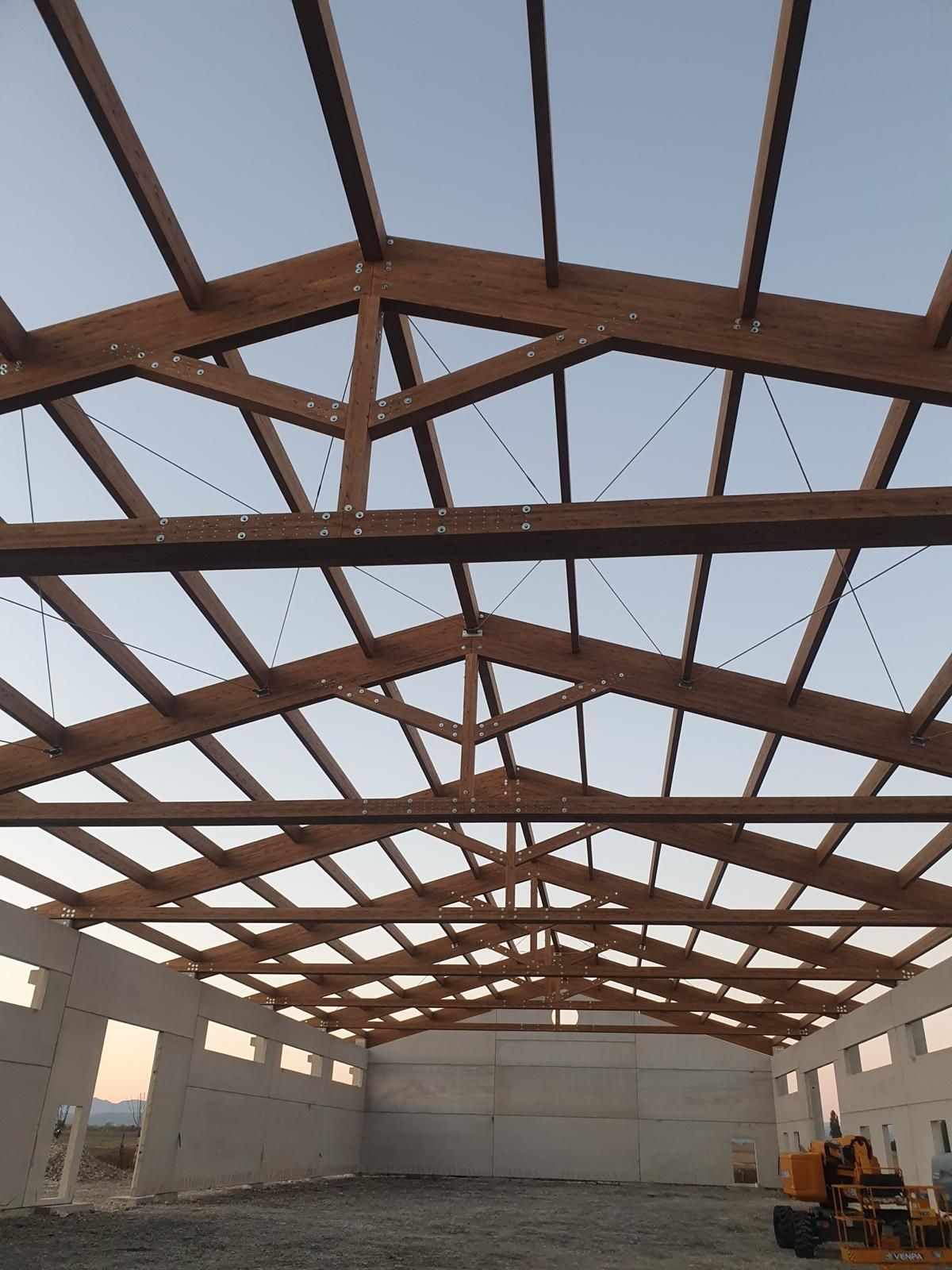 Interno di un edificio in costruzione caratterizzato da una struttura del tetto in legno sopra pareti in cemento di colore chiaro.