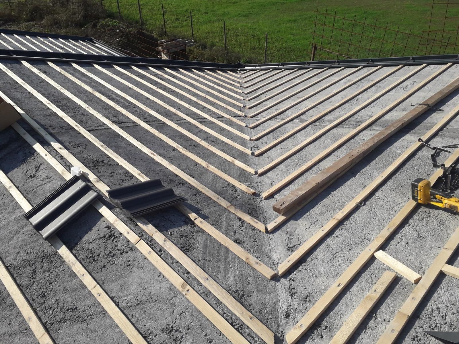 Vista dall'alto di un tetto in costruzione, con sottostrato Riwega verde, listelli di legno e grondaie in rame.