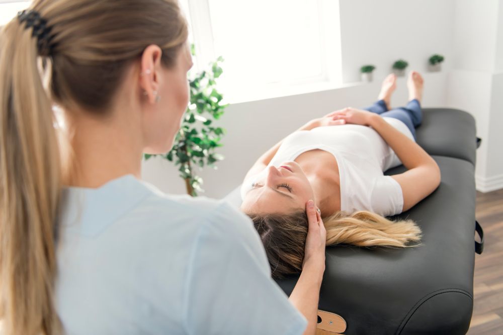 A Woman is Laying on a Table Getting a Head Massage From a Nurse — Body In Motion Physiotherapy In Pialba, QLD