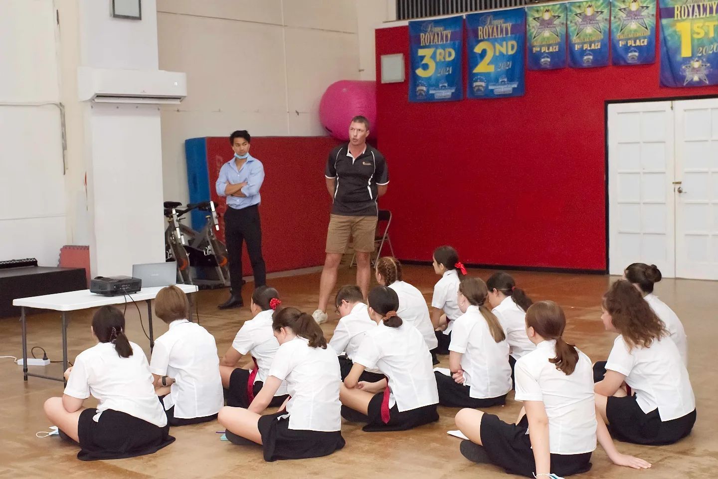 A group of children sit on the floor in front of a man giving a presentation