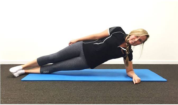 A woman is doing a side plank on a yoga mat.
