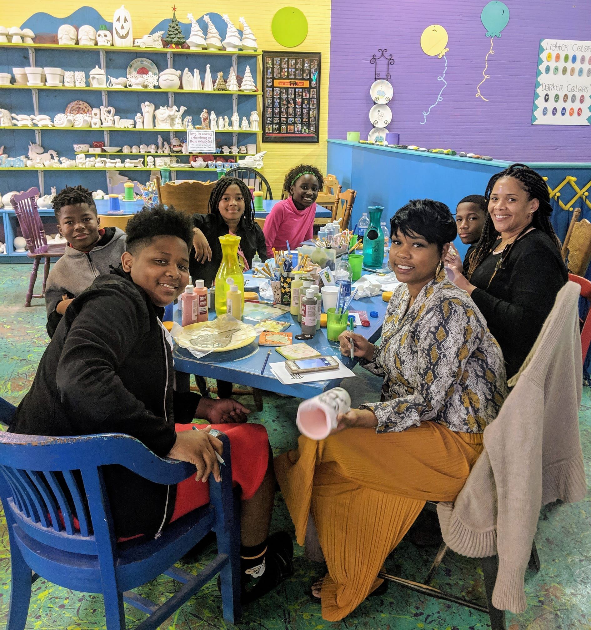 Group of people at a craft table, painting ceramics in a colorful art studio.