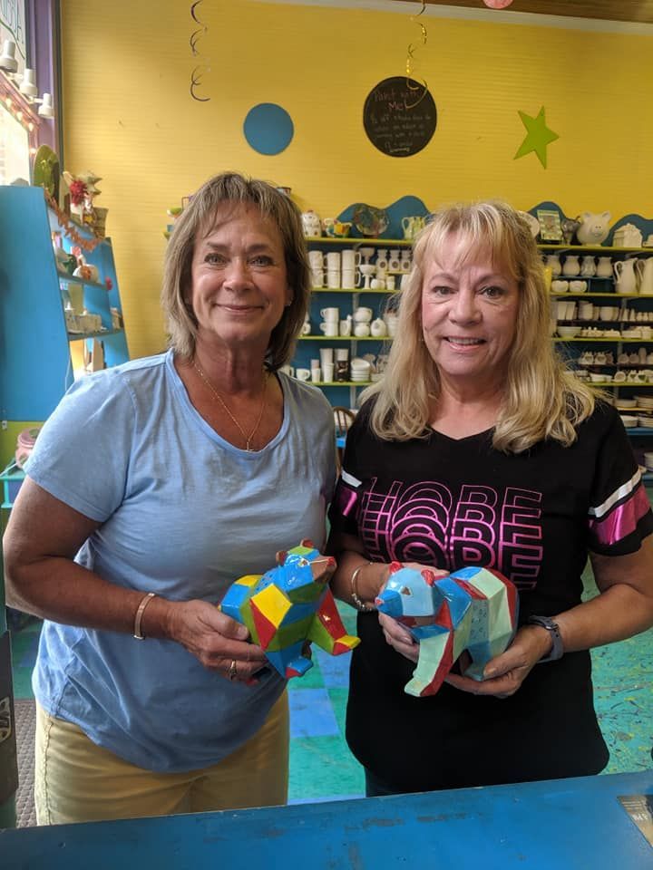 Two women holding colorful geometric animal sculptures in an art studio.