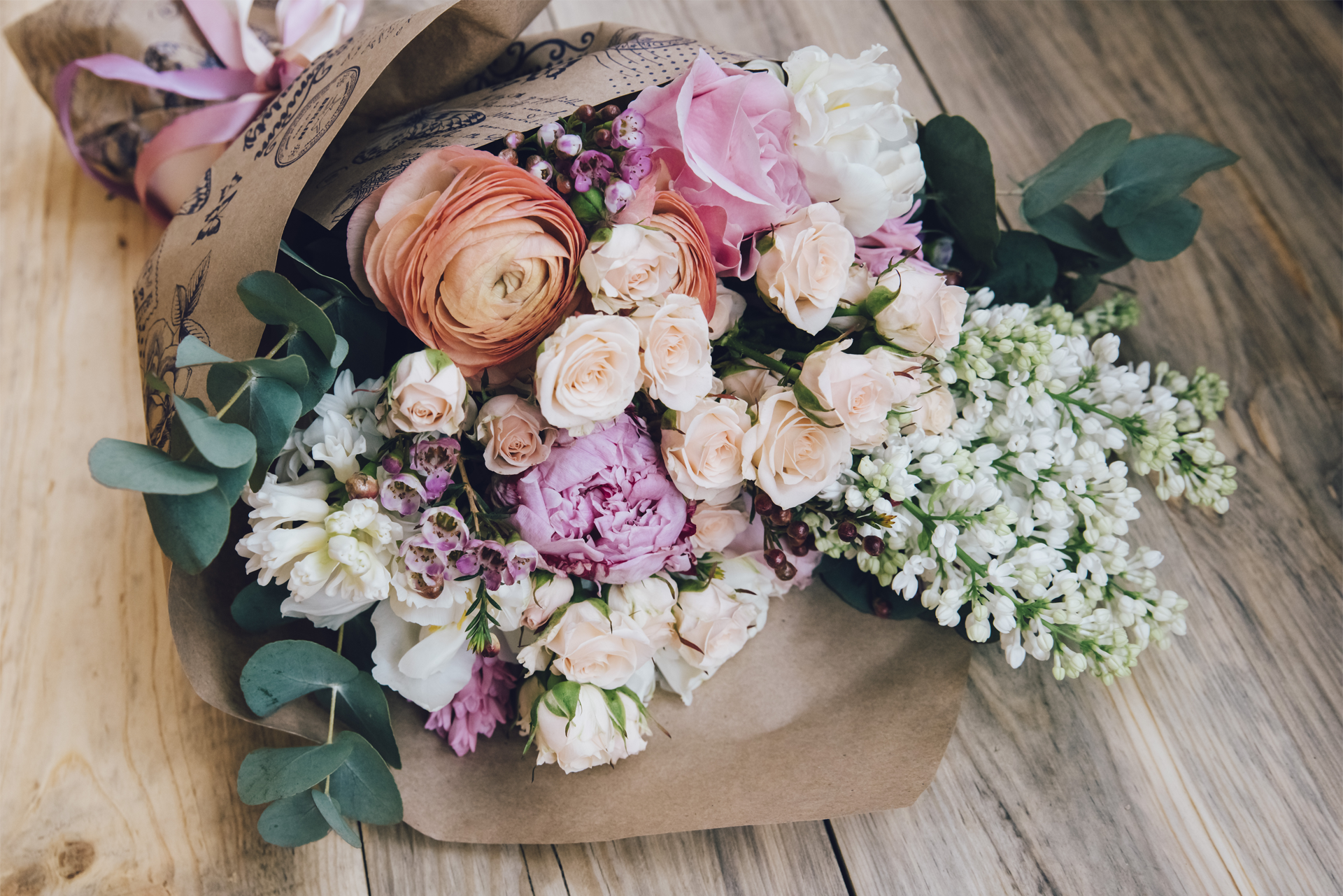 A bouquet of flowers wrapped in brown paper is sitting on a wooden table.