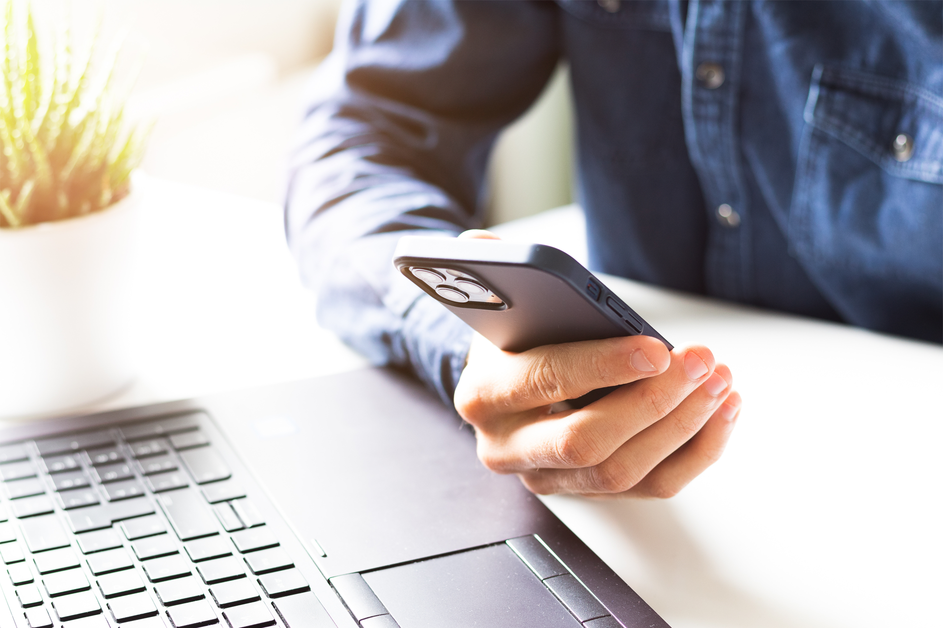 A person is holding a cell phone in front of a laptop.