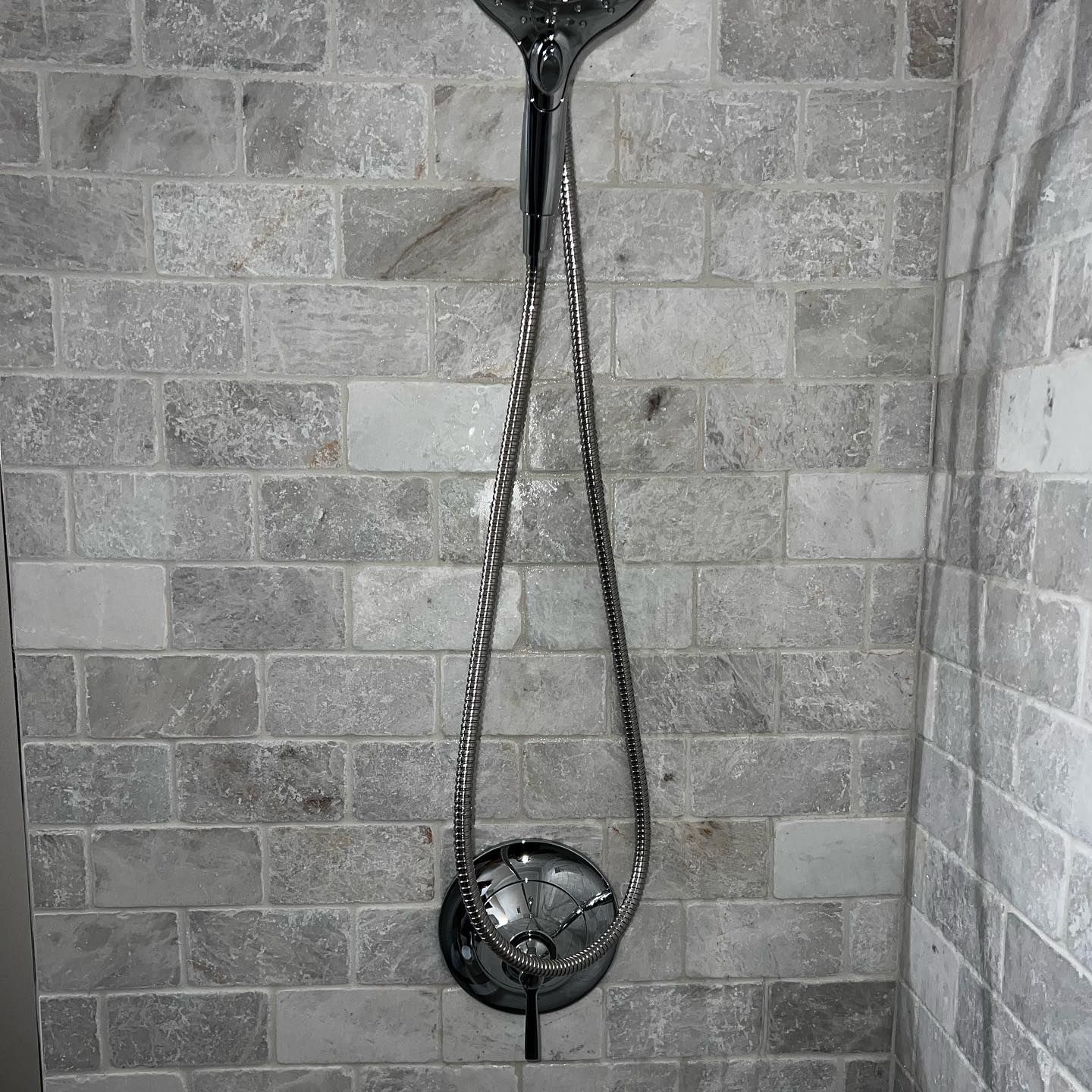 Shower with silver fixtures on a gray and white brick tile wall.