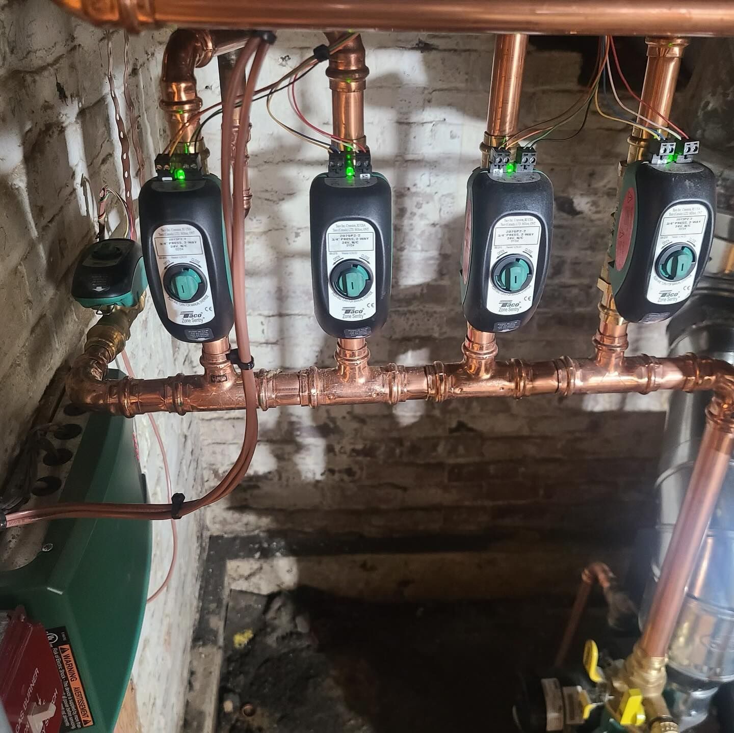 Copper plumbing with four black zone valves, in a basement setting.