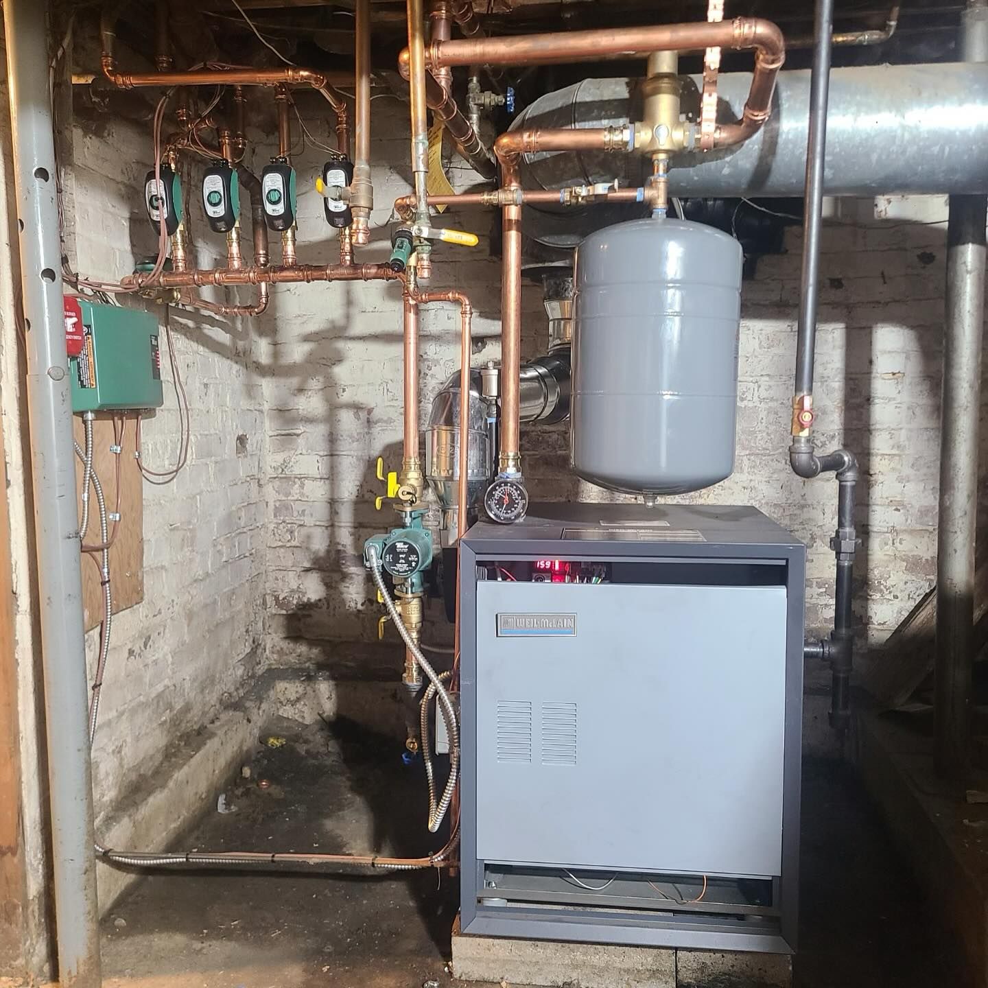 Copper pipes and furnace in a basement setting. A green box and gray expansion tank are visible.
