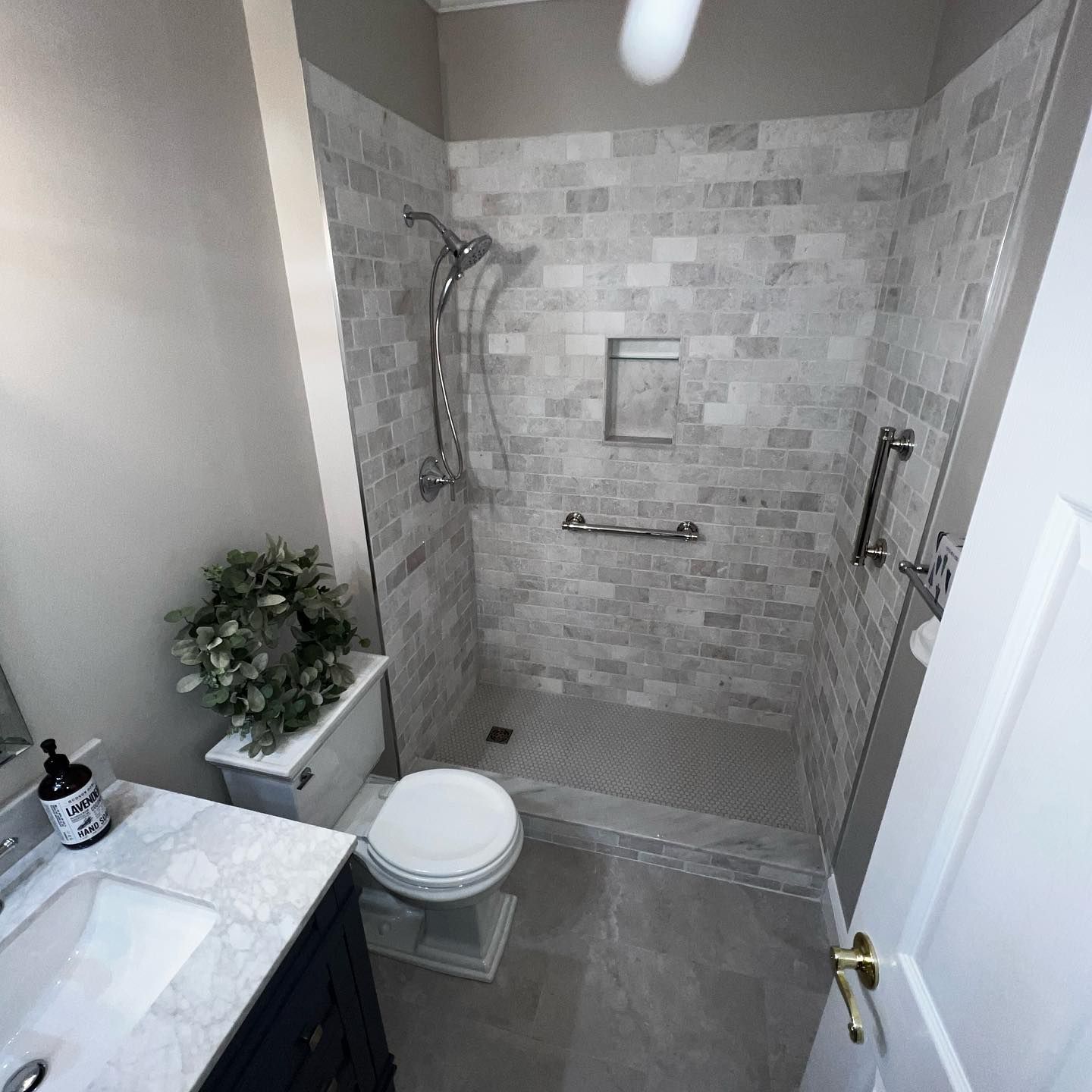 Bathroom with a gray tile shower, accessible grab bars, toilet, and sink.