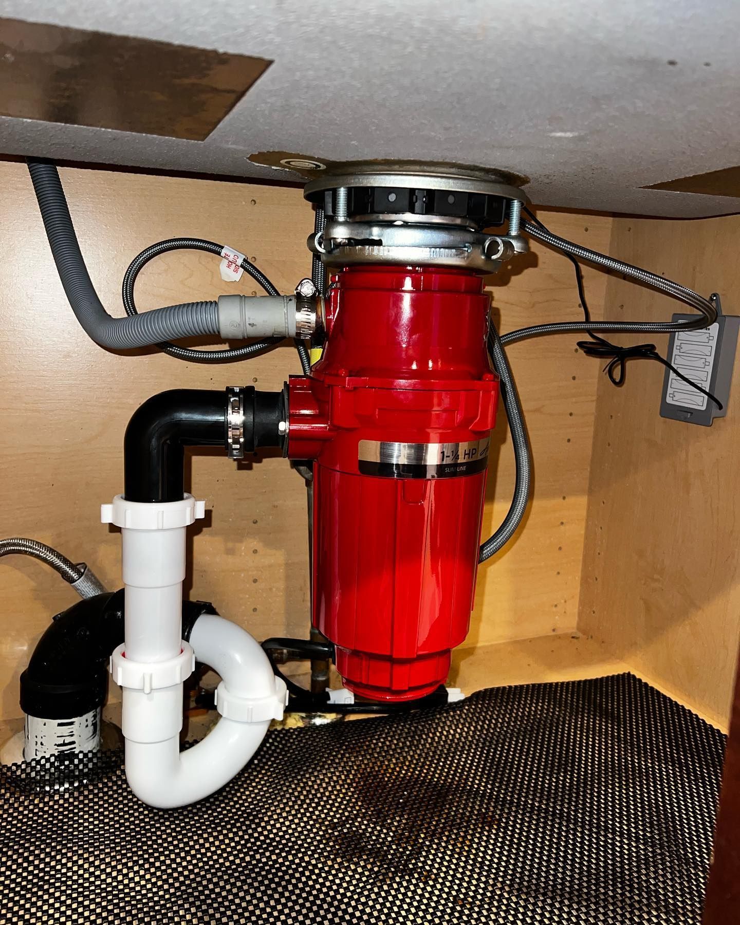Red garbage disposal unit under a kitchen sink with connected plumbing and electrical wiring.