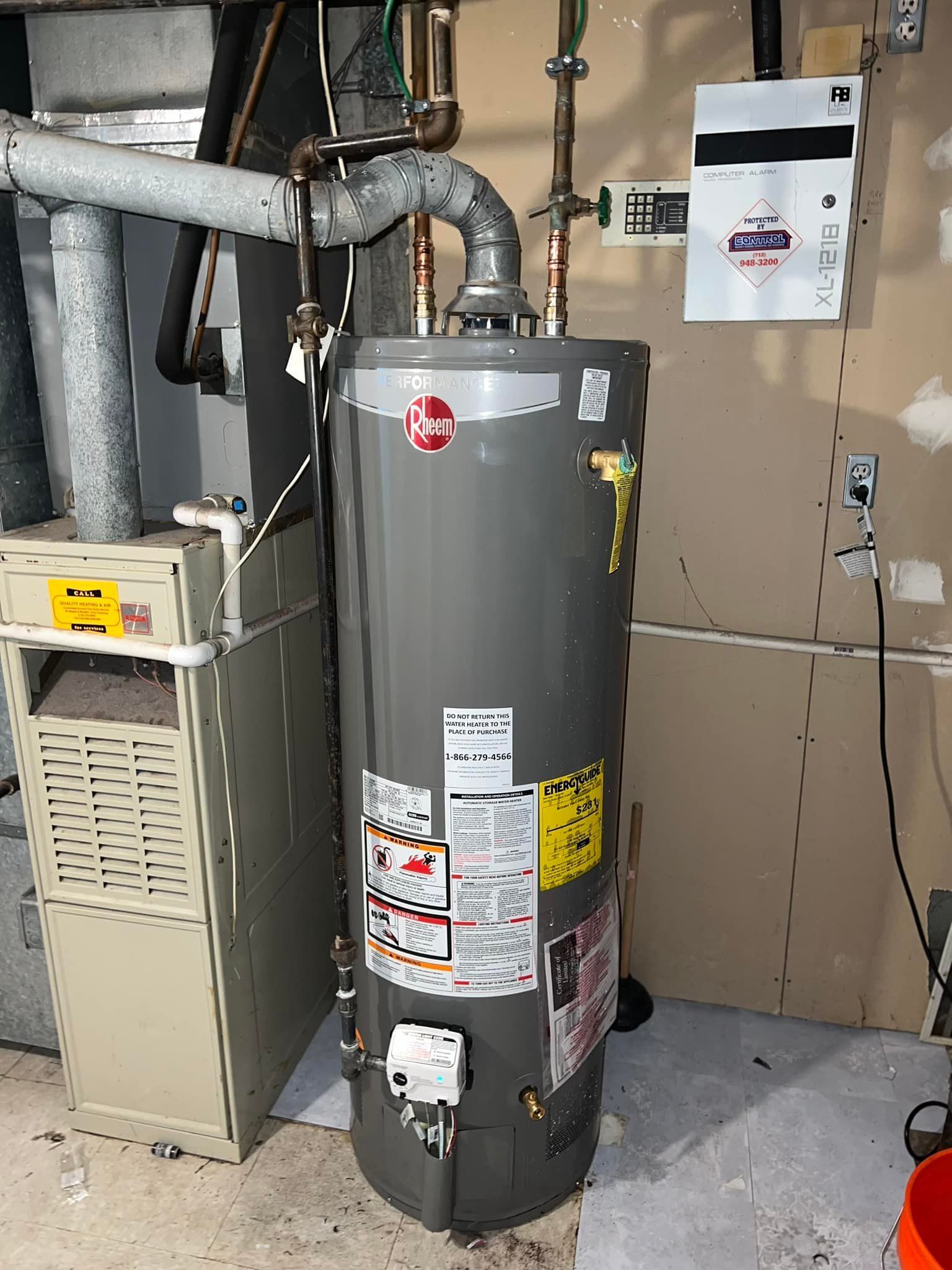 A tall, gray water heater next to a furnace in a basement setting.