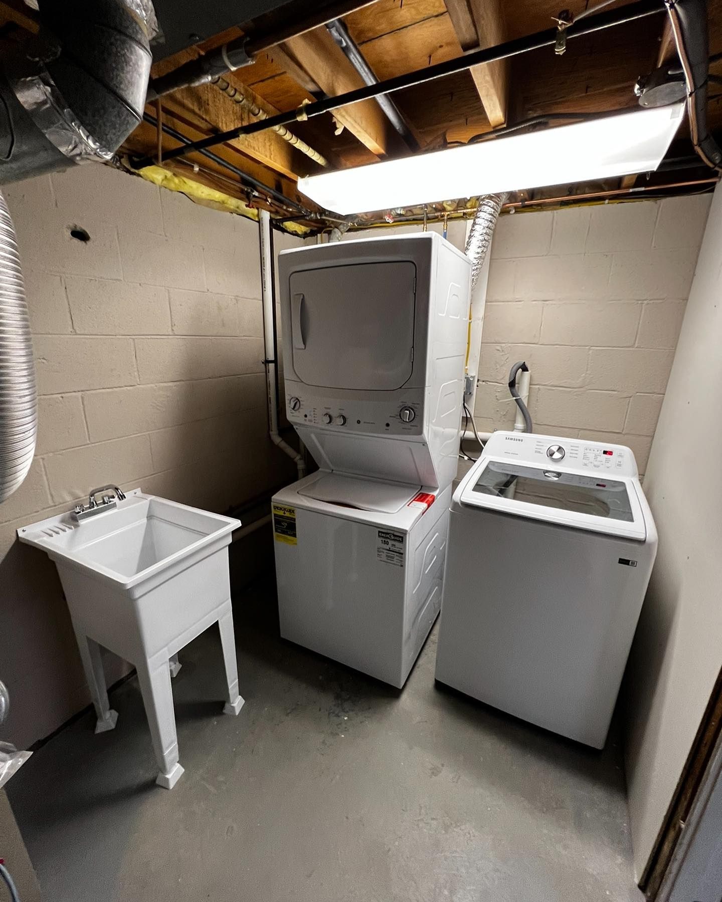 Laundry room with a stacked washer/dryer, a washing machine, and a utility sink.
